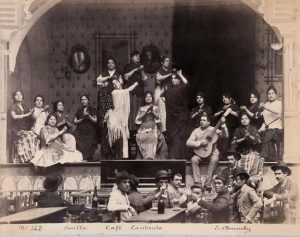 Group of flamenco dancers and musicians in a cafe, performing on a stage.