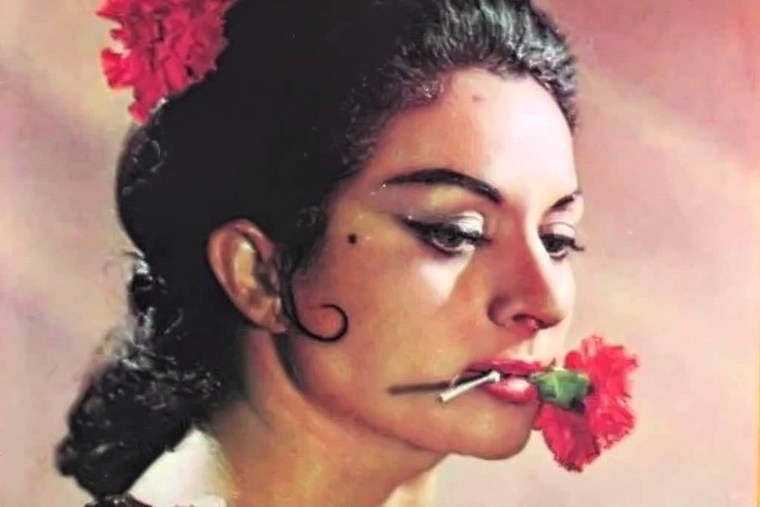 Woman with a red flower in her hair, holding a red flower in her mouth.