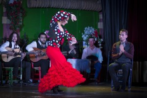 Flamenco dancer in red dress performs with musicians in background.