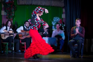 Flamenco dancer in red dress with musicians playing guitar on stage.