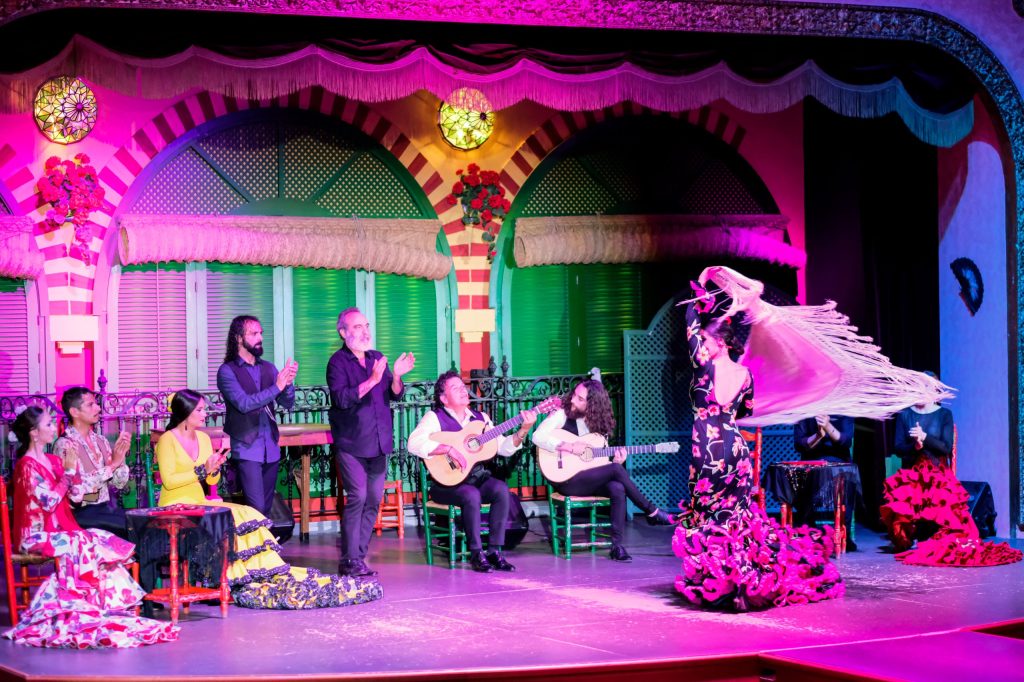 Flamenco performance with dancers, musicians, and colorful stage lighting.