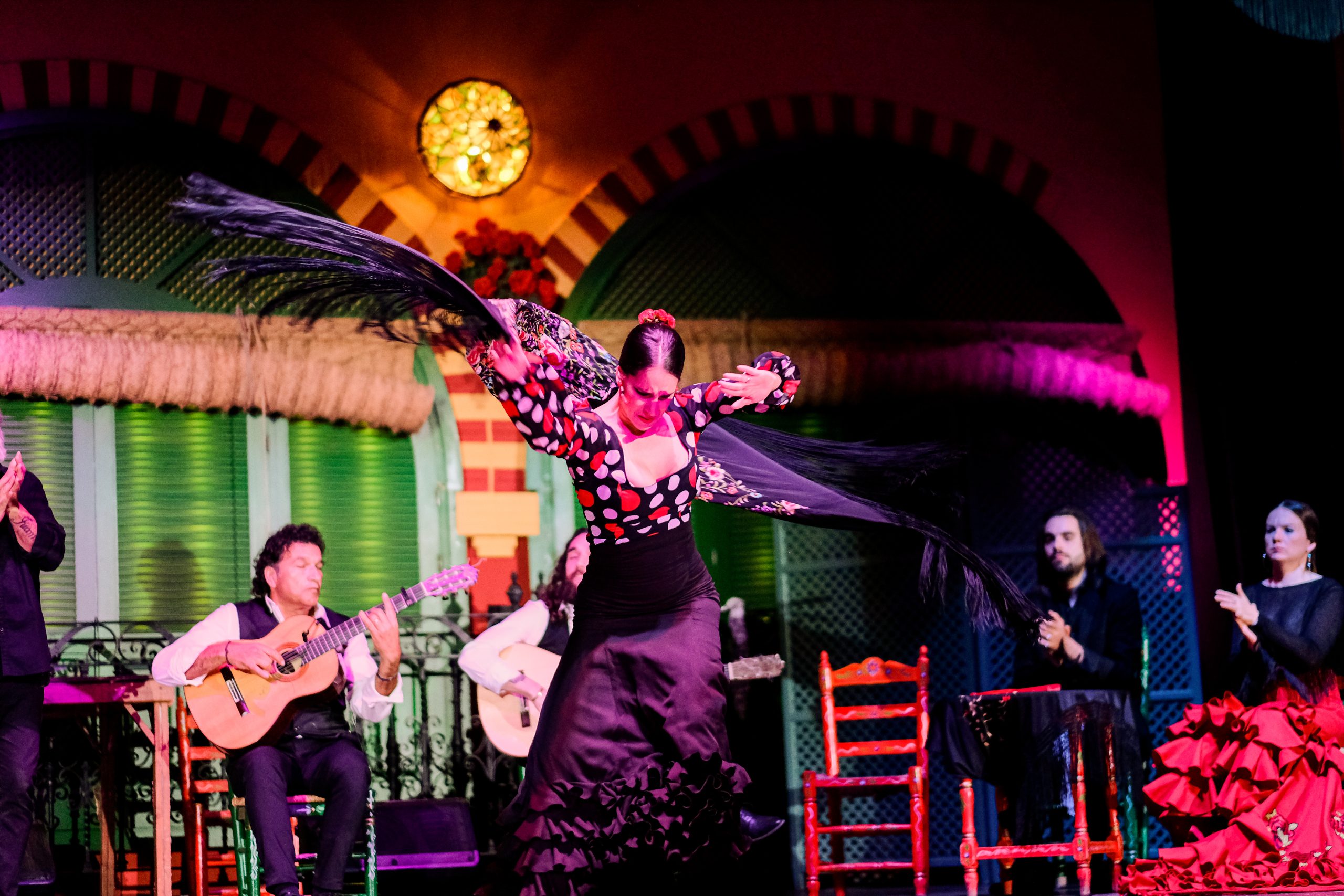 Flamenco dancer in vibrant dress performs with musicians on stage.