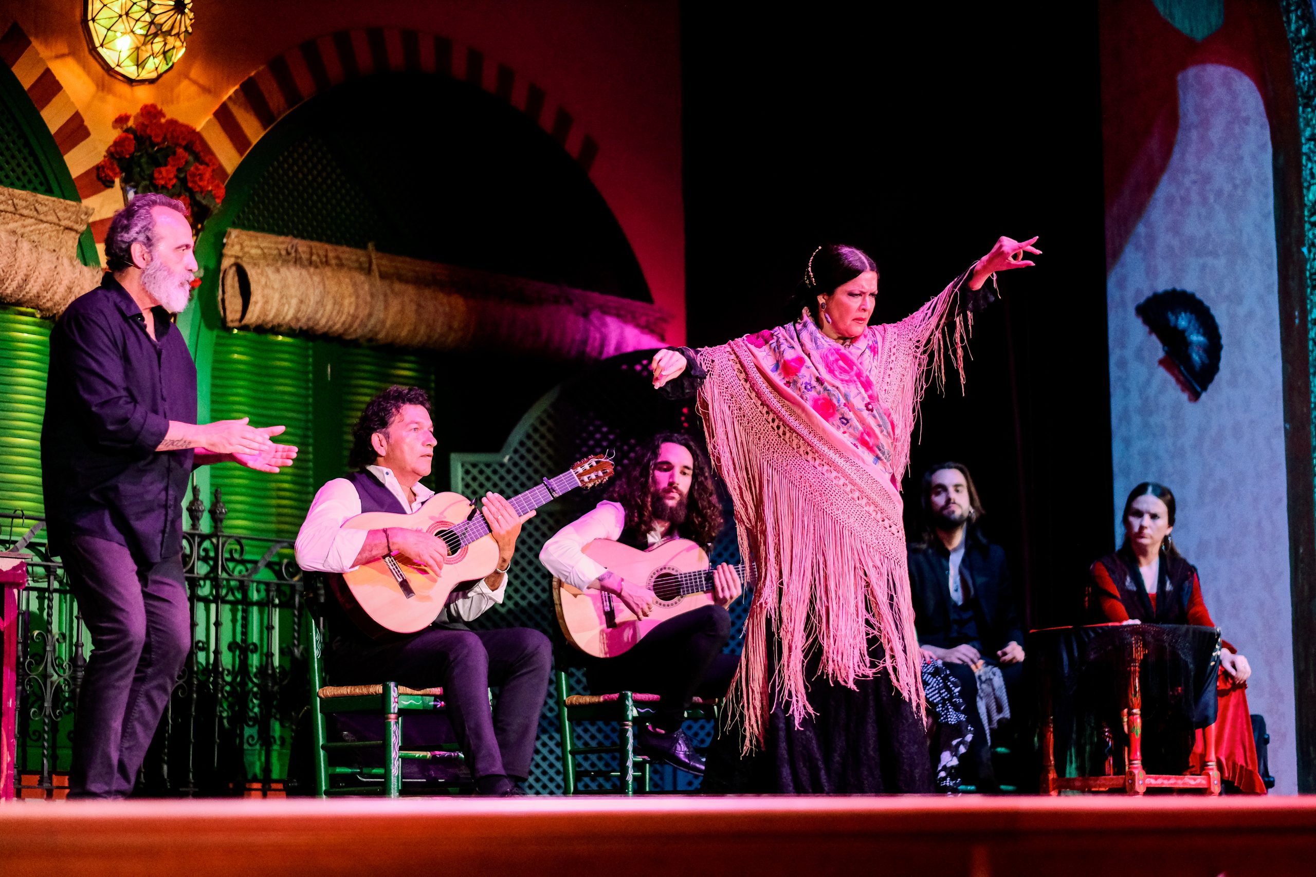 Flamenco dancer performs with musicians playing guitars on stage.