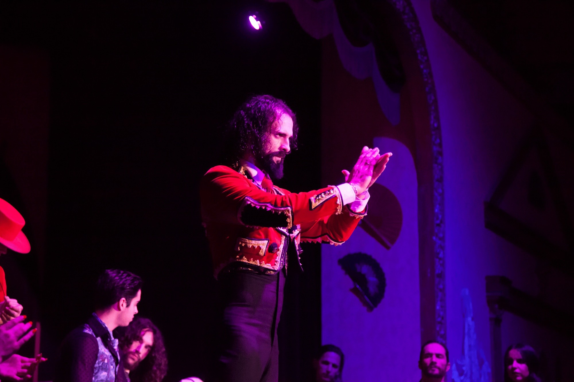 Man in red suit clapping on stage under purple light.