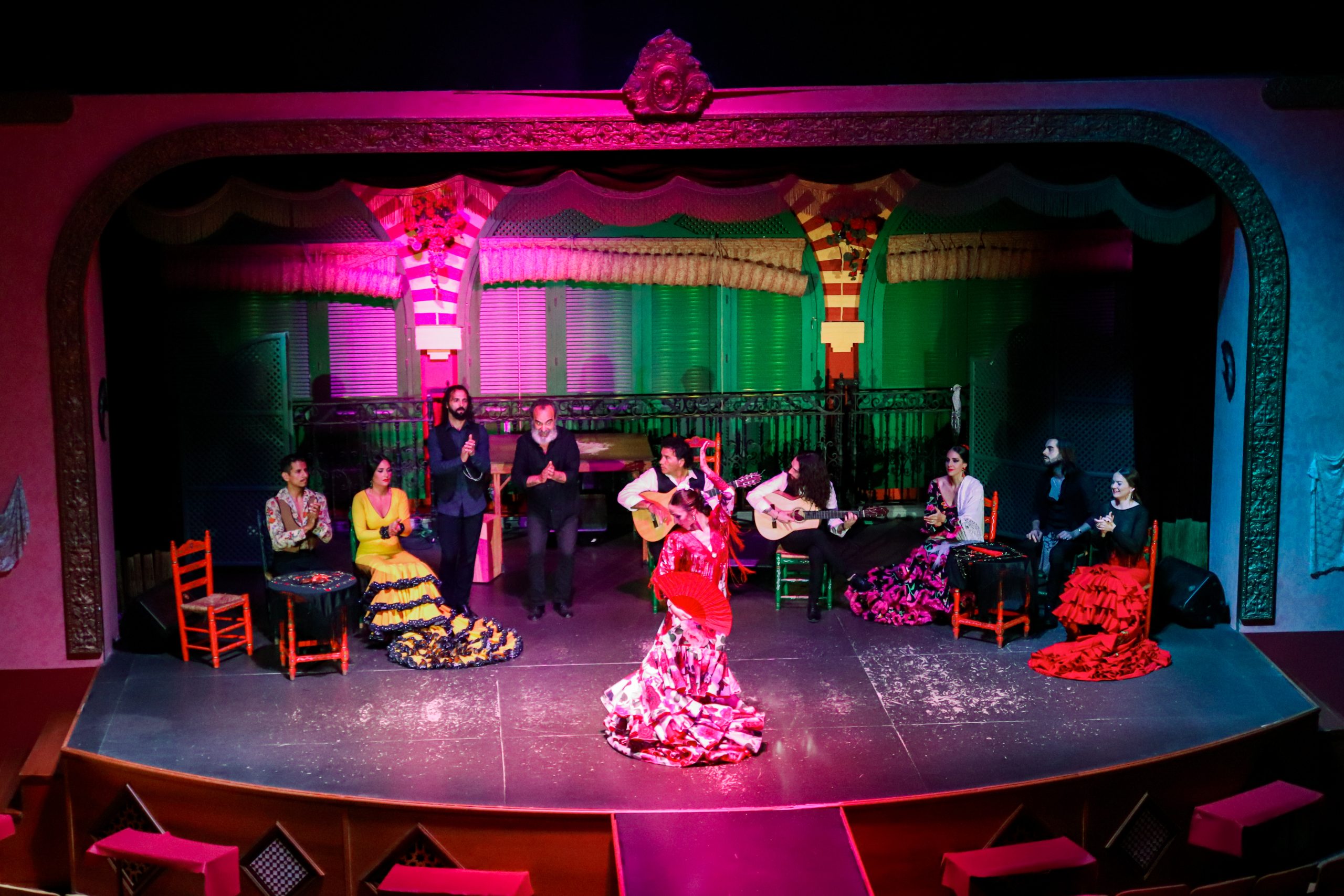 Flamenco dancers and musicians performing on a colorful stage with vibrant costumes.