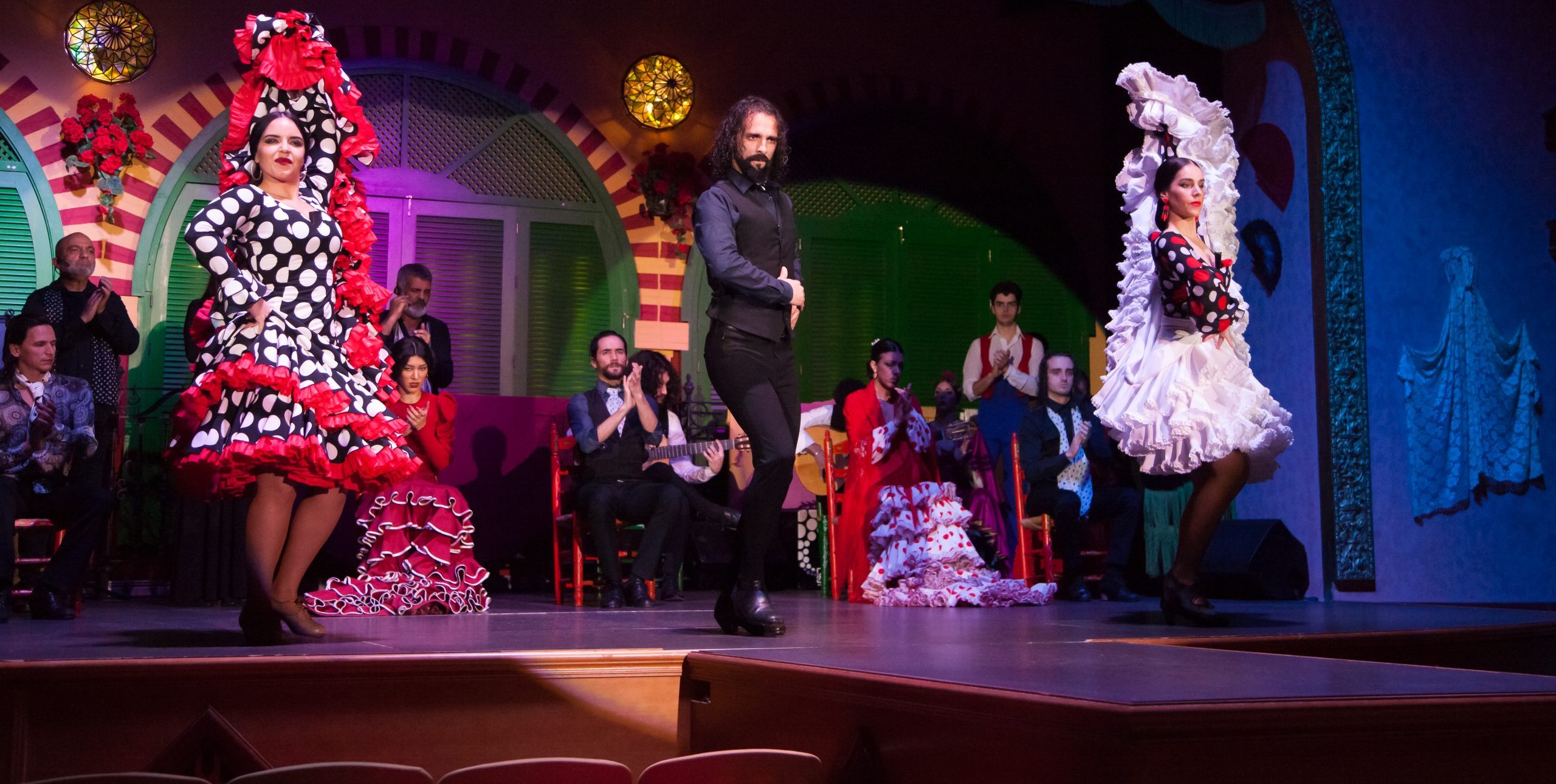 Three flamenco dancers performing on stage with musicians in the background.