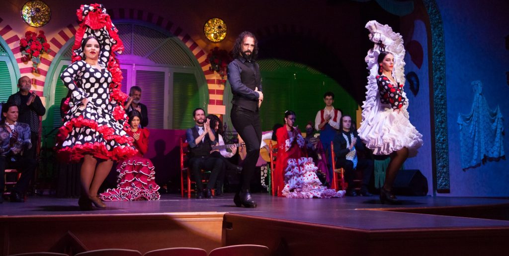 Three flamenco dancers performing on stage with musicians in the background.