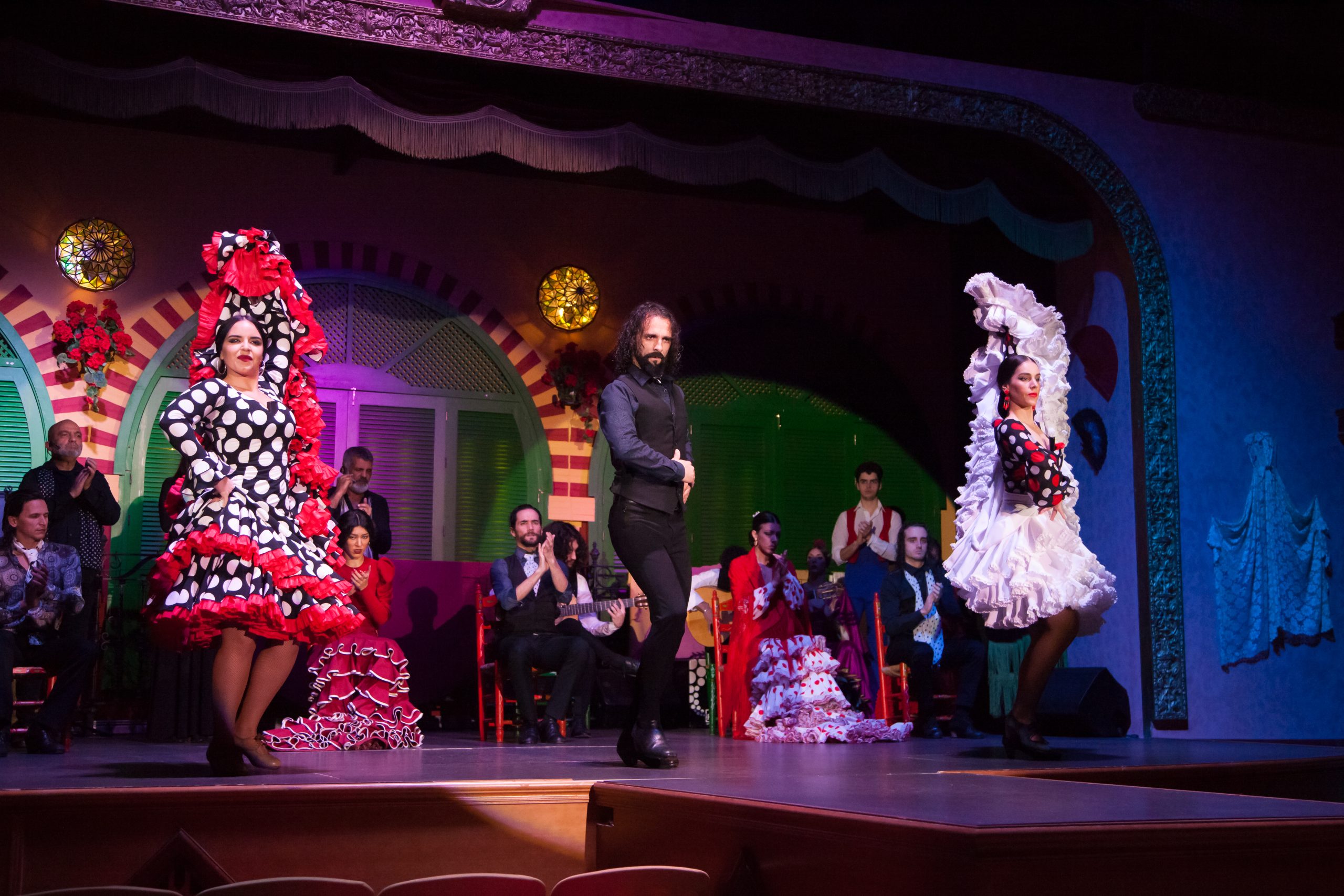 Three flamenco dancers performing on stage with musicians in the background.
