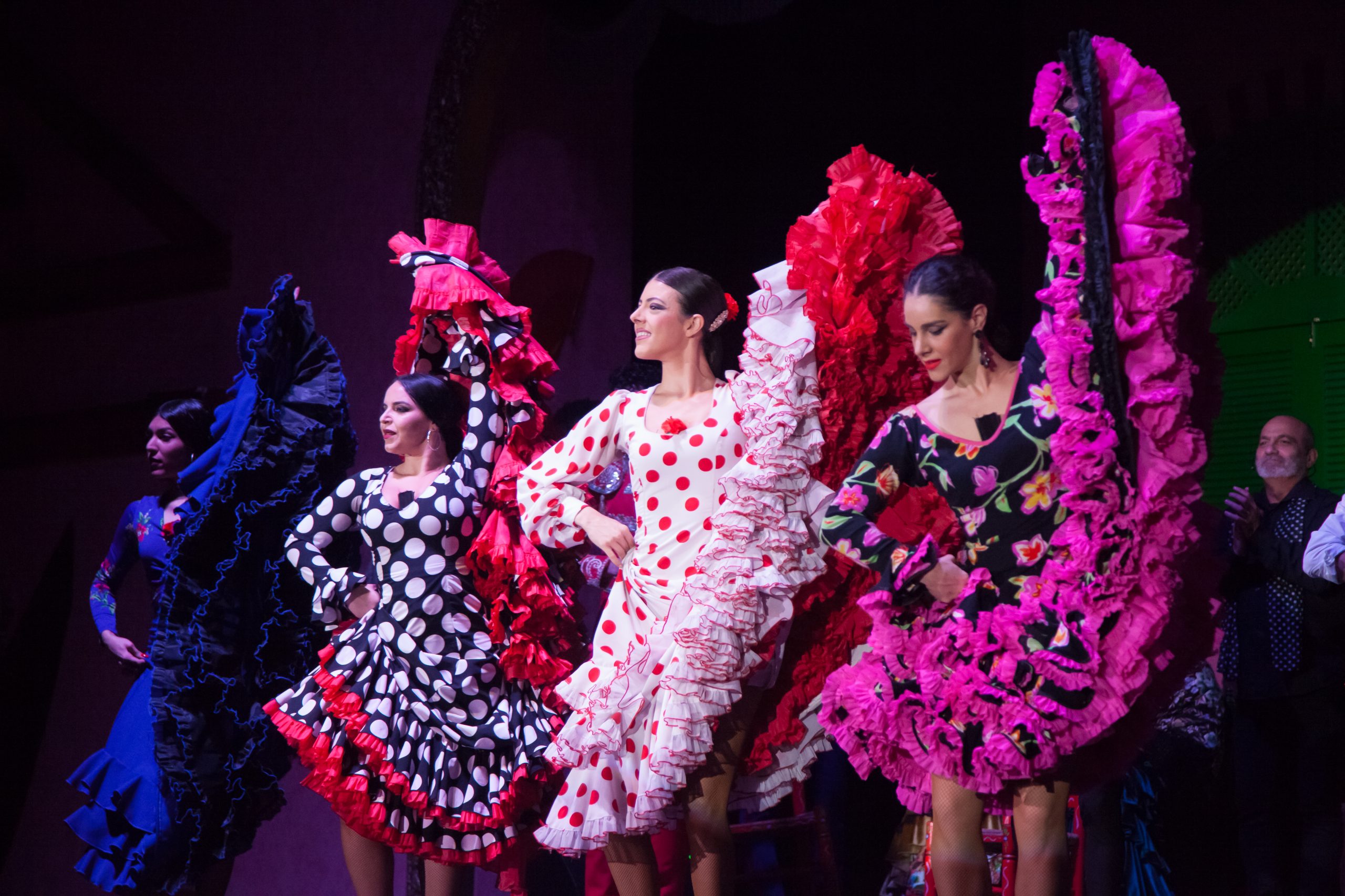 Women in colorful flamenco dresses dancing on stage.