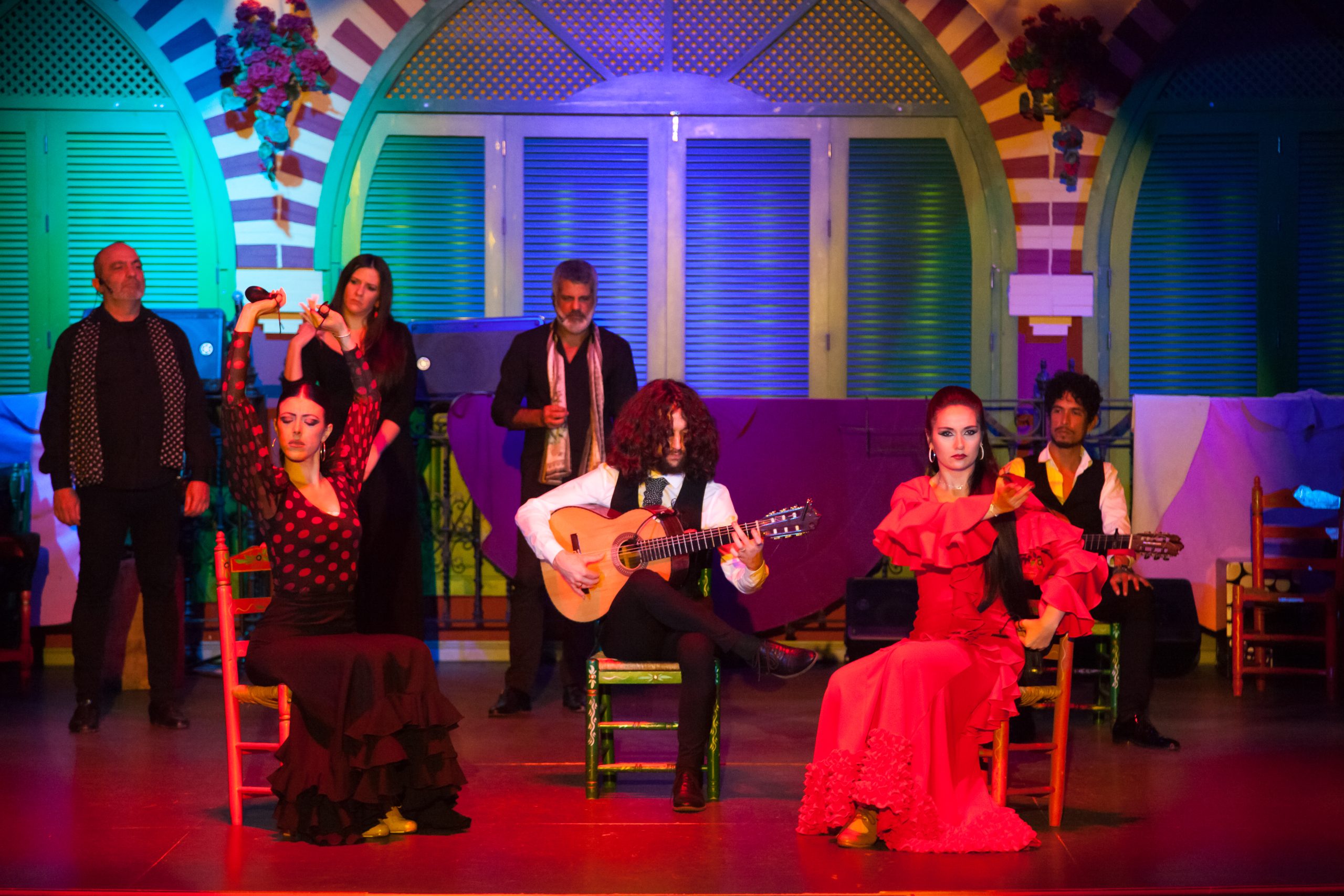 Flamenco dancers and guitarists perform on a colorful stage.