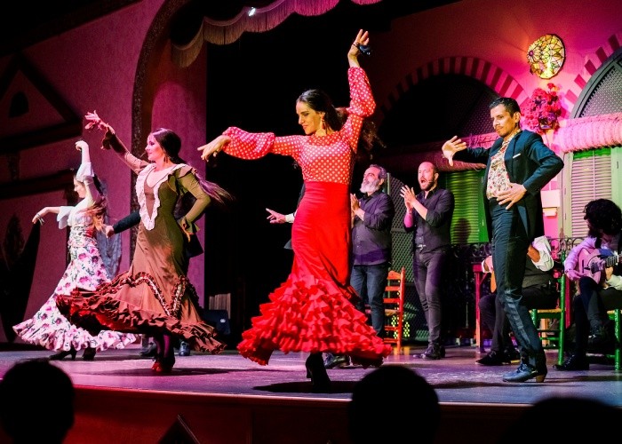 Flamenco dancers in vibrant costumes perform on stage with musicians.