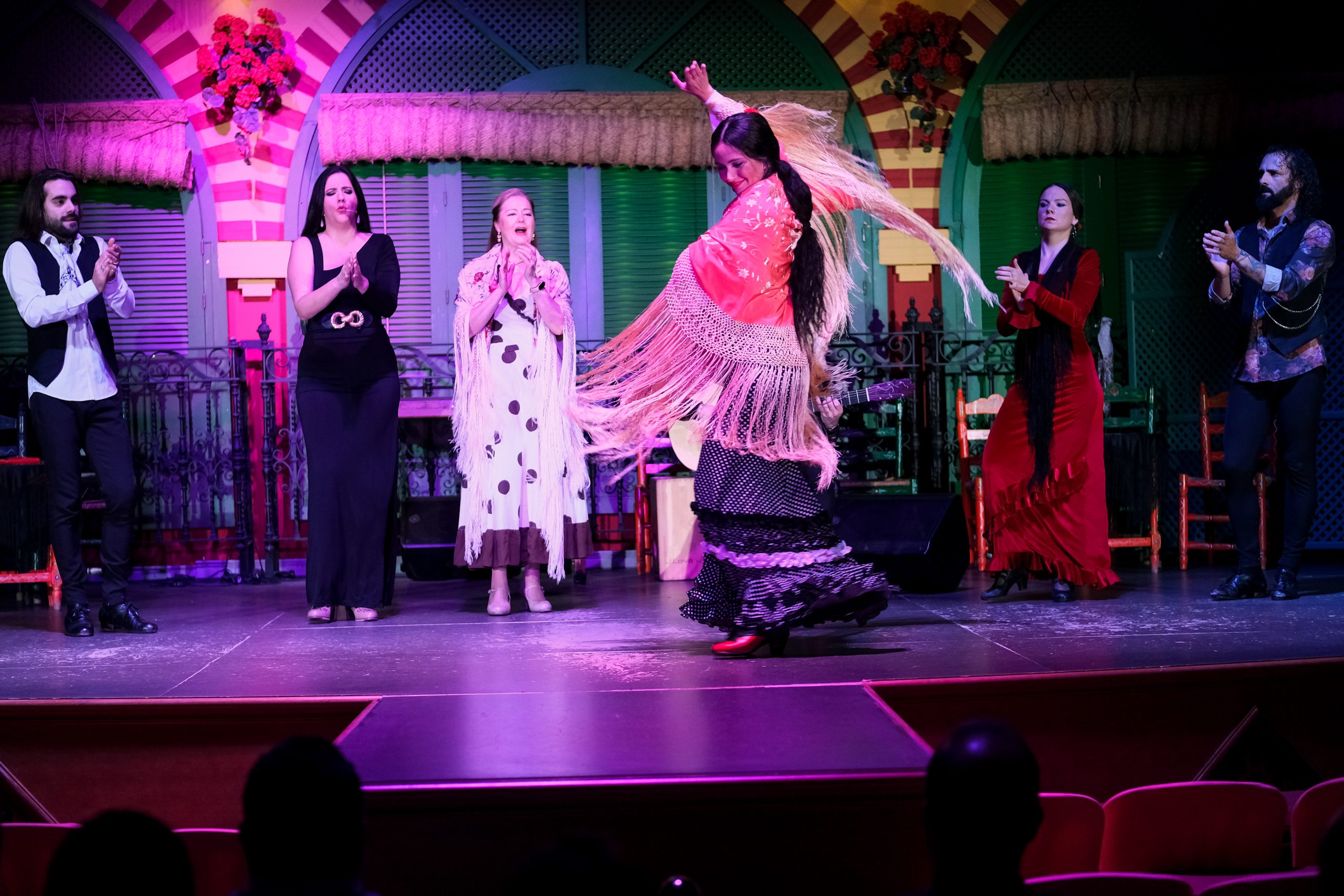 Flamenco dancers on stage with colorful costumes and vibrant backdrop.