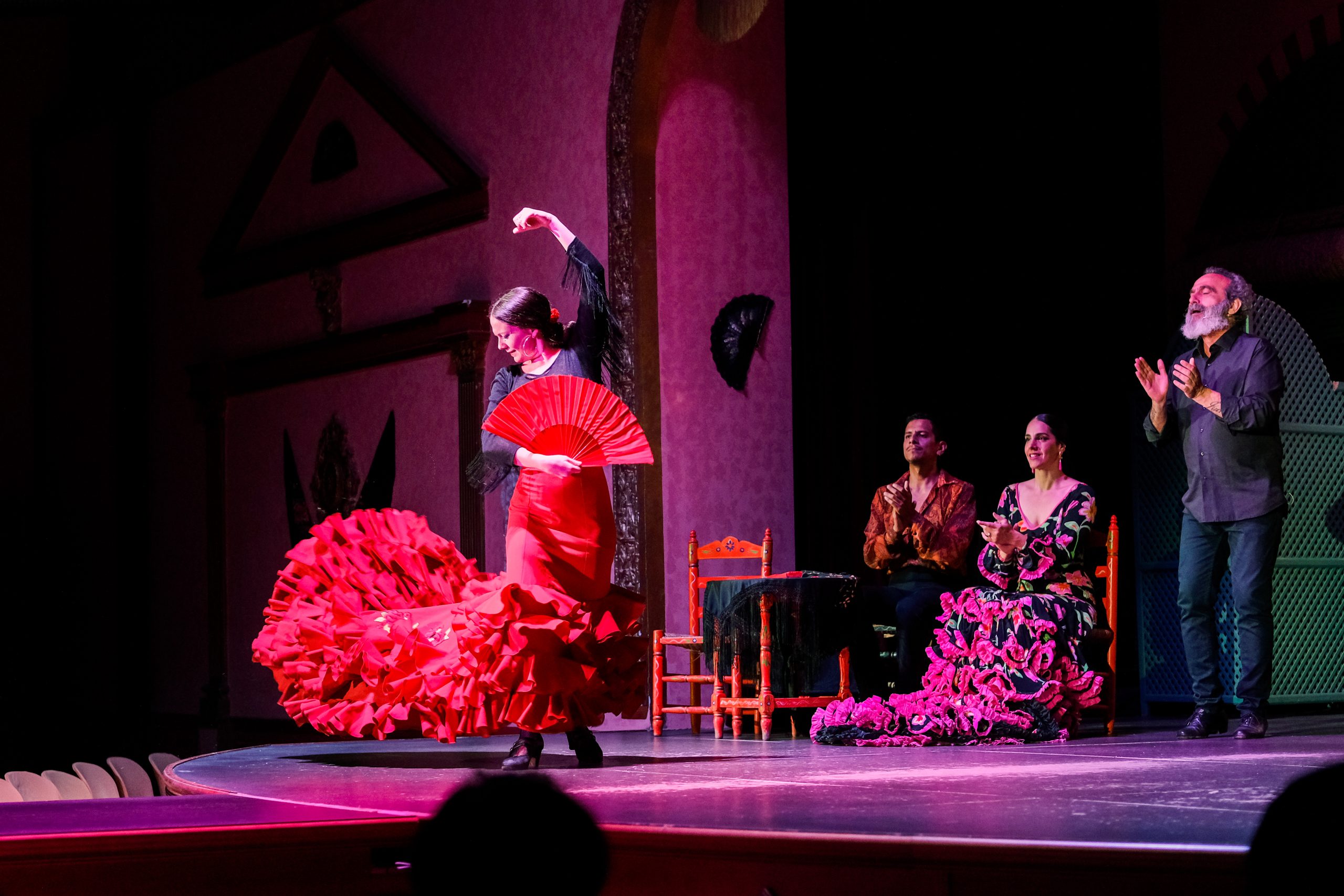 Flamenco dancer in red dress performing with three musicians on stage.