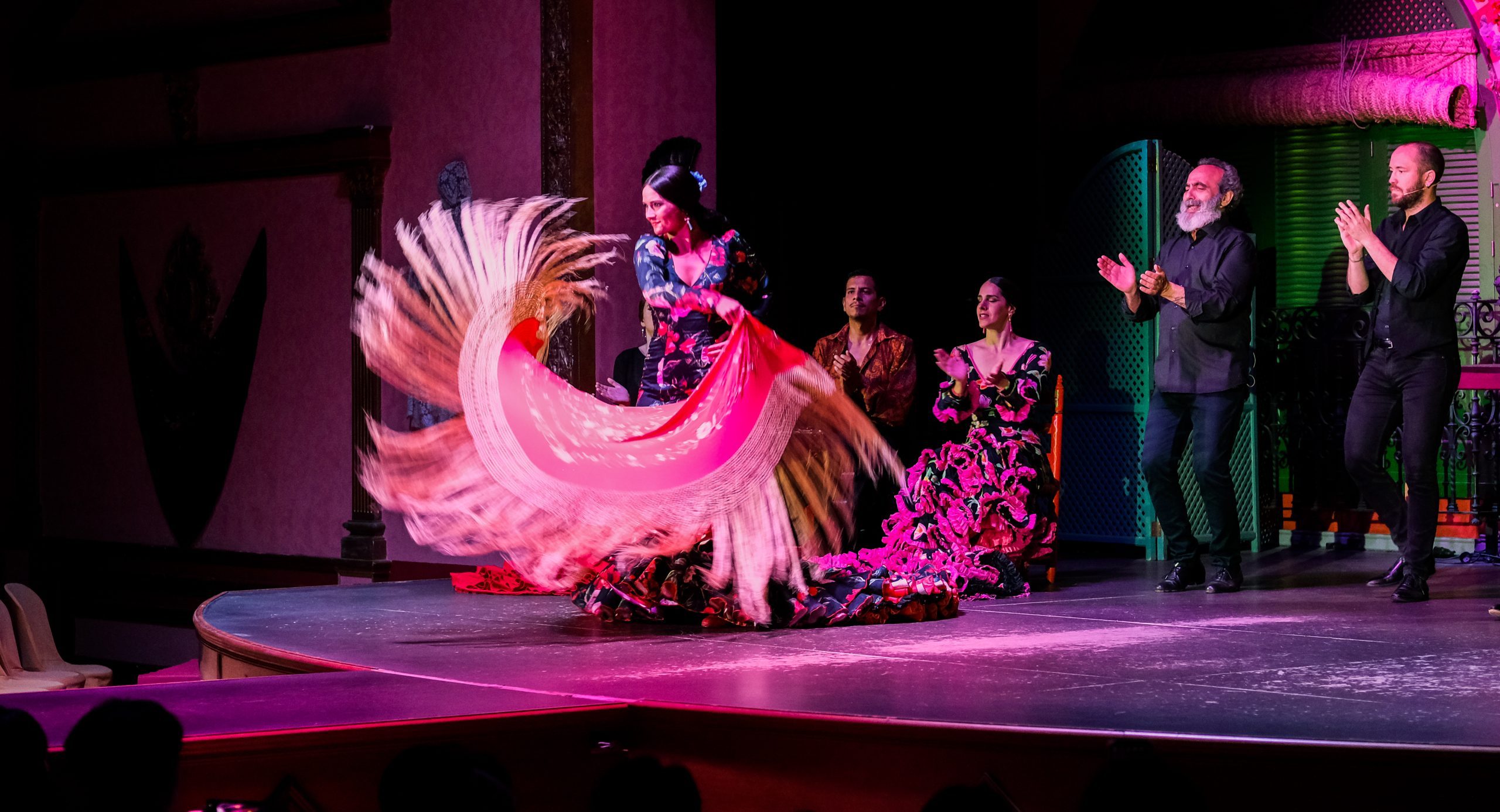 Flamenco dancers perform energetically on a stage with colorful dresses and a swirling shawl.