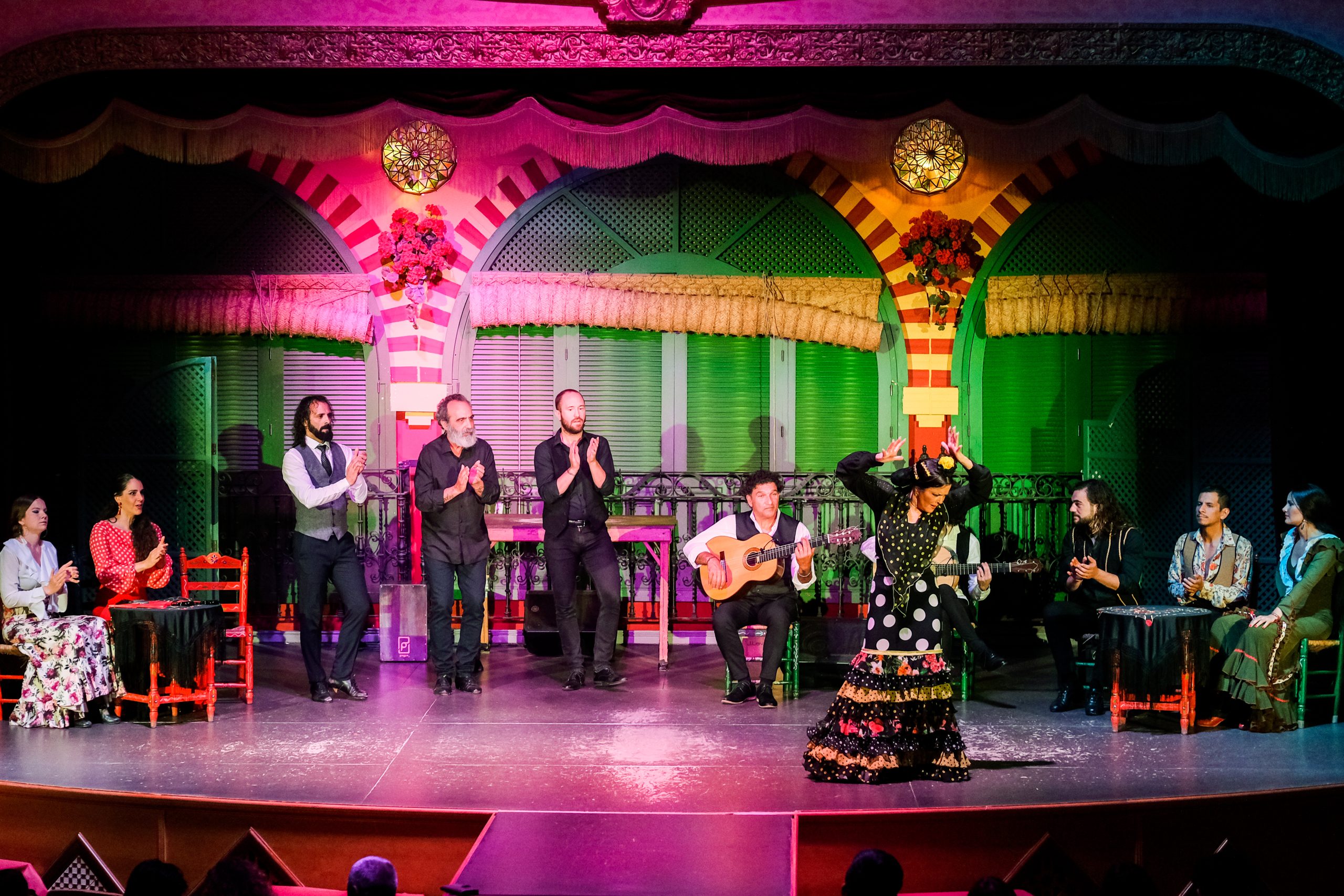 Flamenco dance performance on stage with musicians and dancers in colorful costumes.