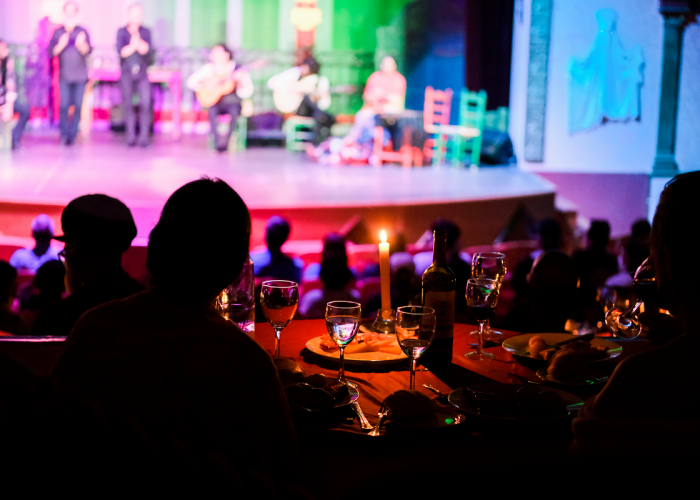 Silhouettes dining with a colorful stage show in the background.