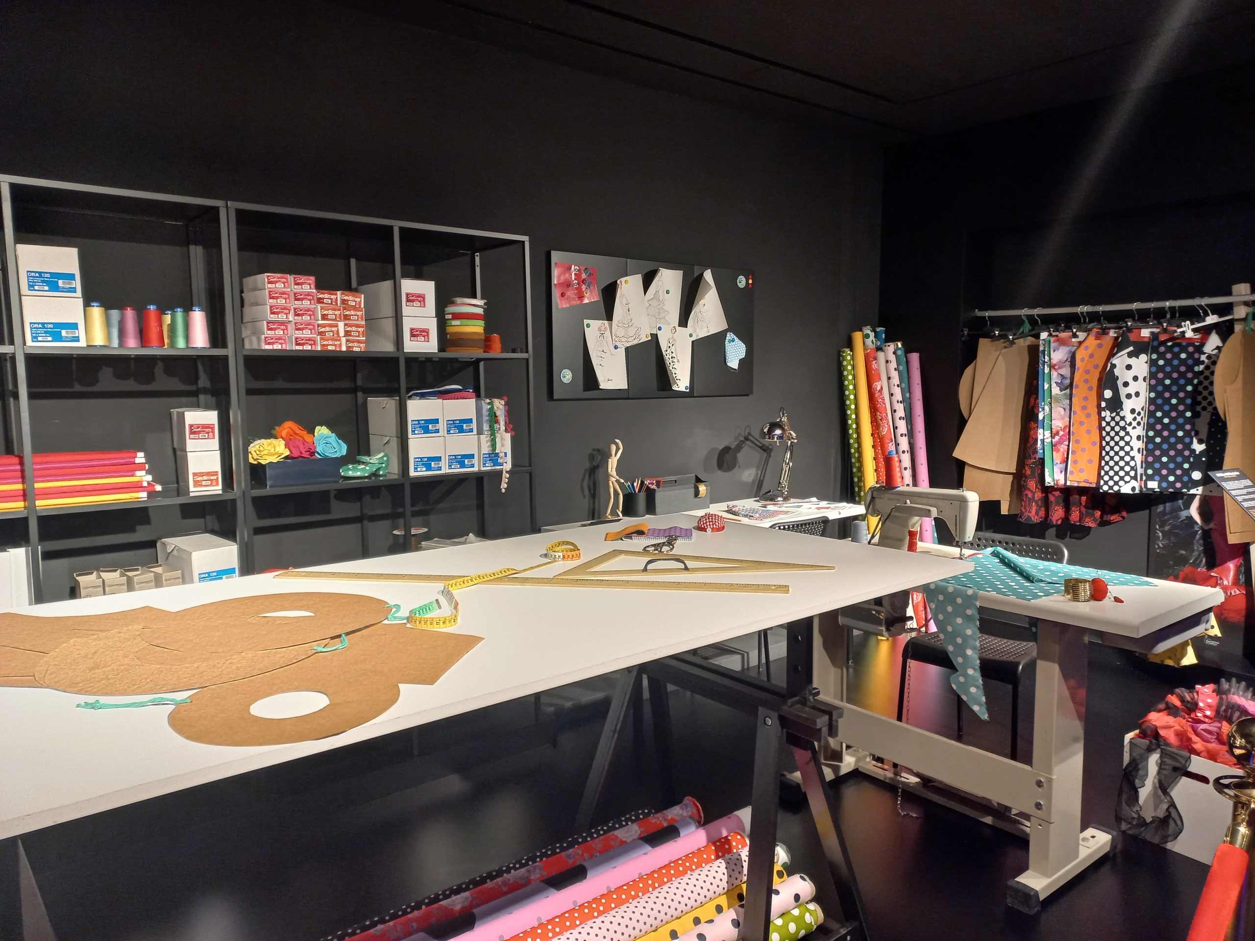 Sewing studio with patterns, fabric rolls, and sewing tools on tables and shelves.
