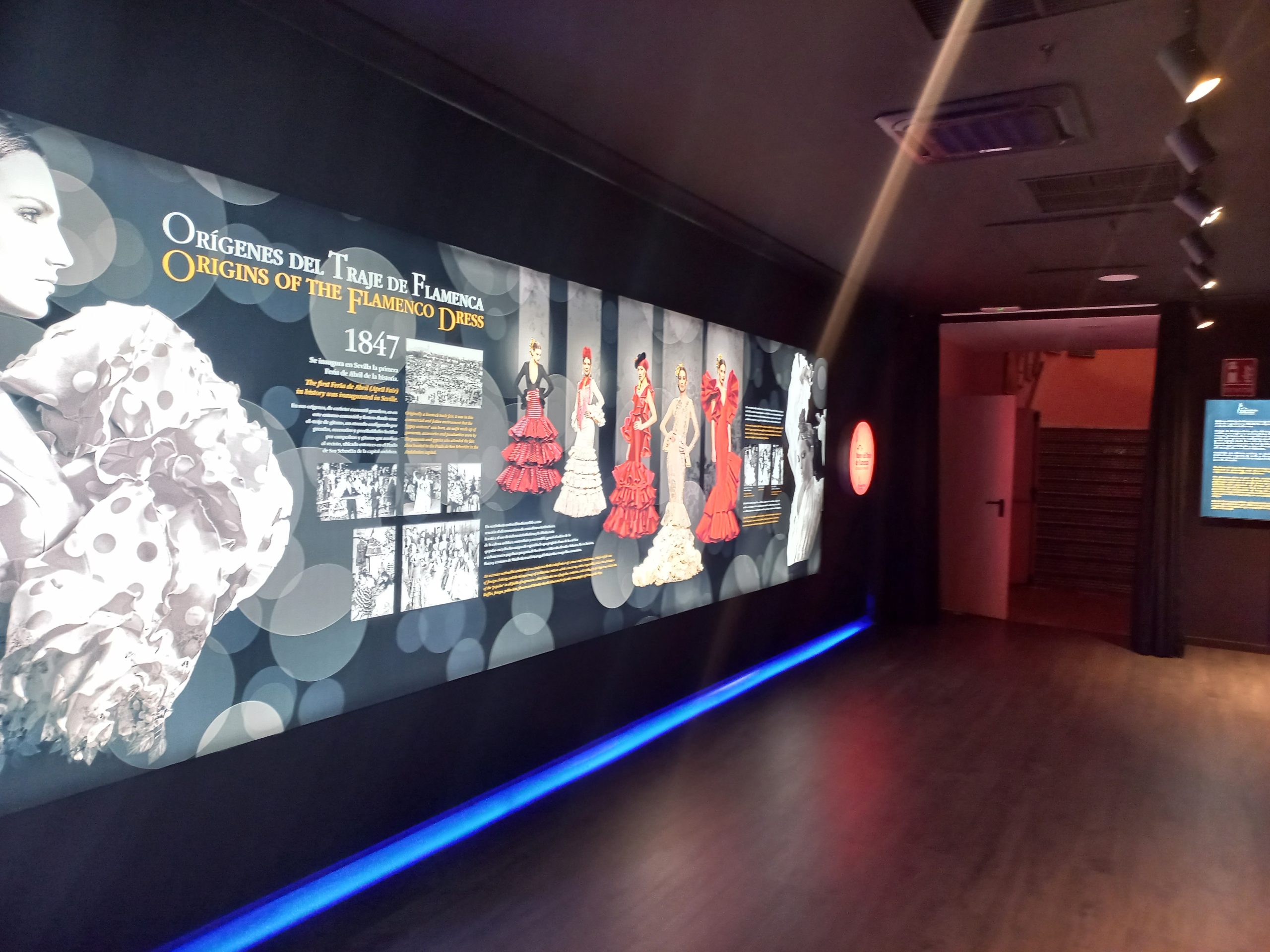 Museum exhibit on flamenco dresses with images and text on a long wall display.