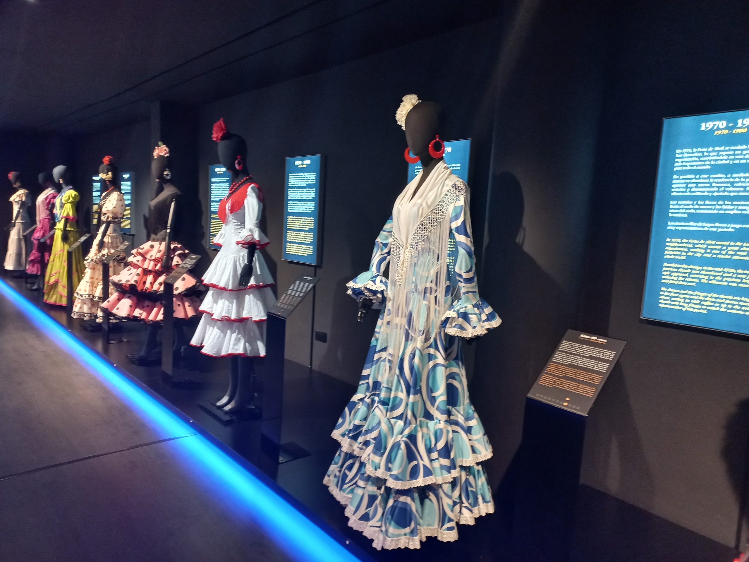 Exhibit of mannequins dressed in colorful flamenco dresses in a dimly lit museum.