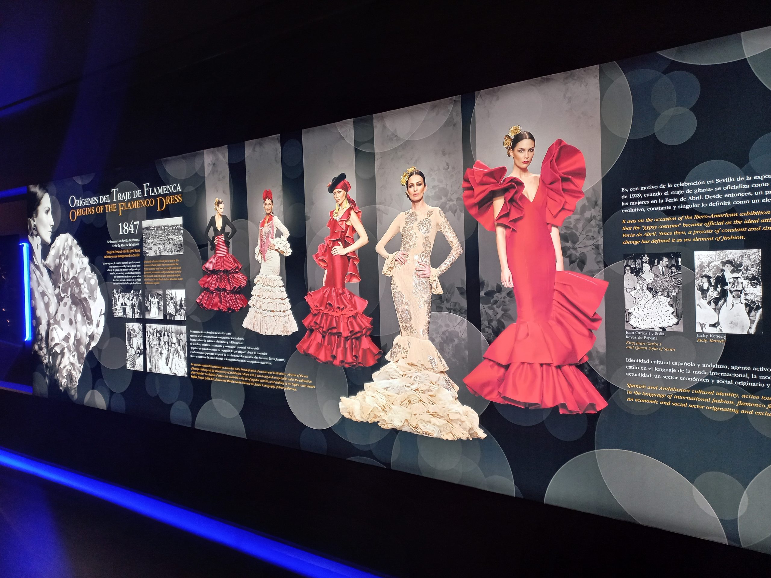 Exhibit display of flamenco dresses with historical text and images.