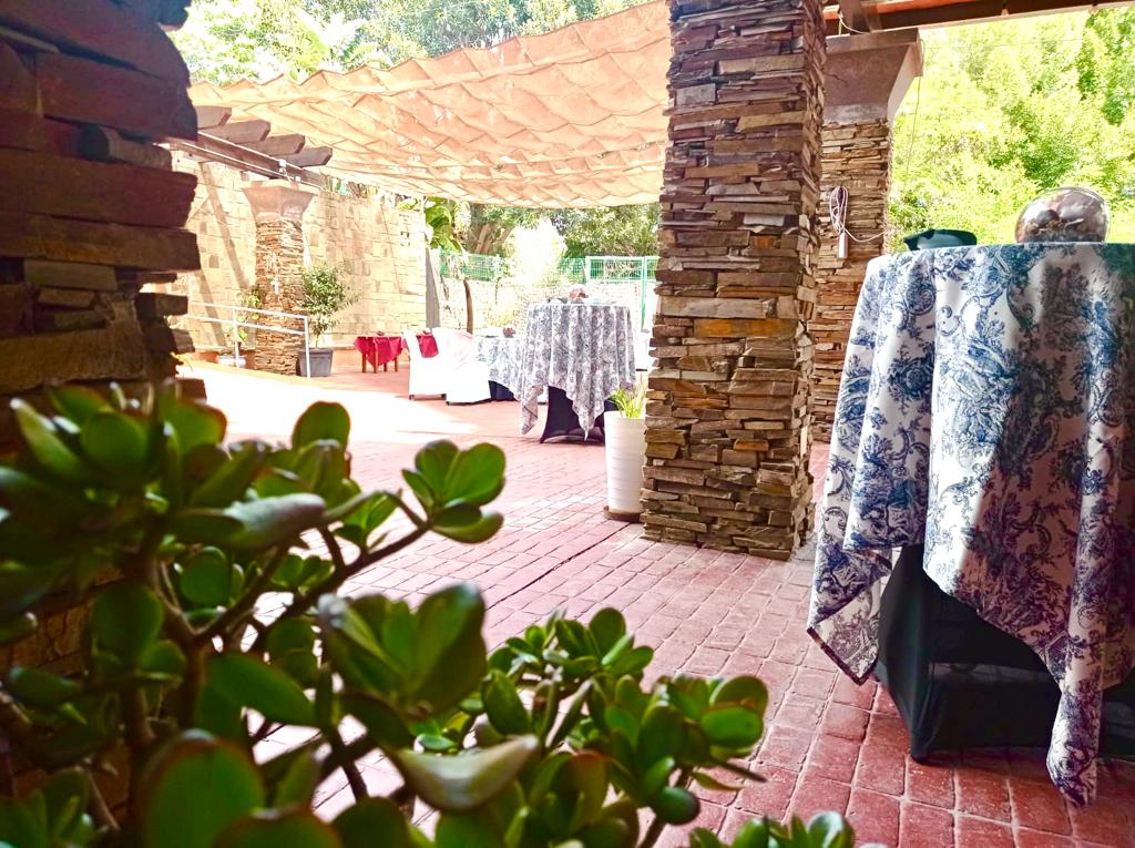 Outdoor patio with plants and tables covered with patterned cloth.