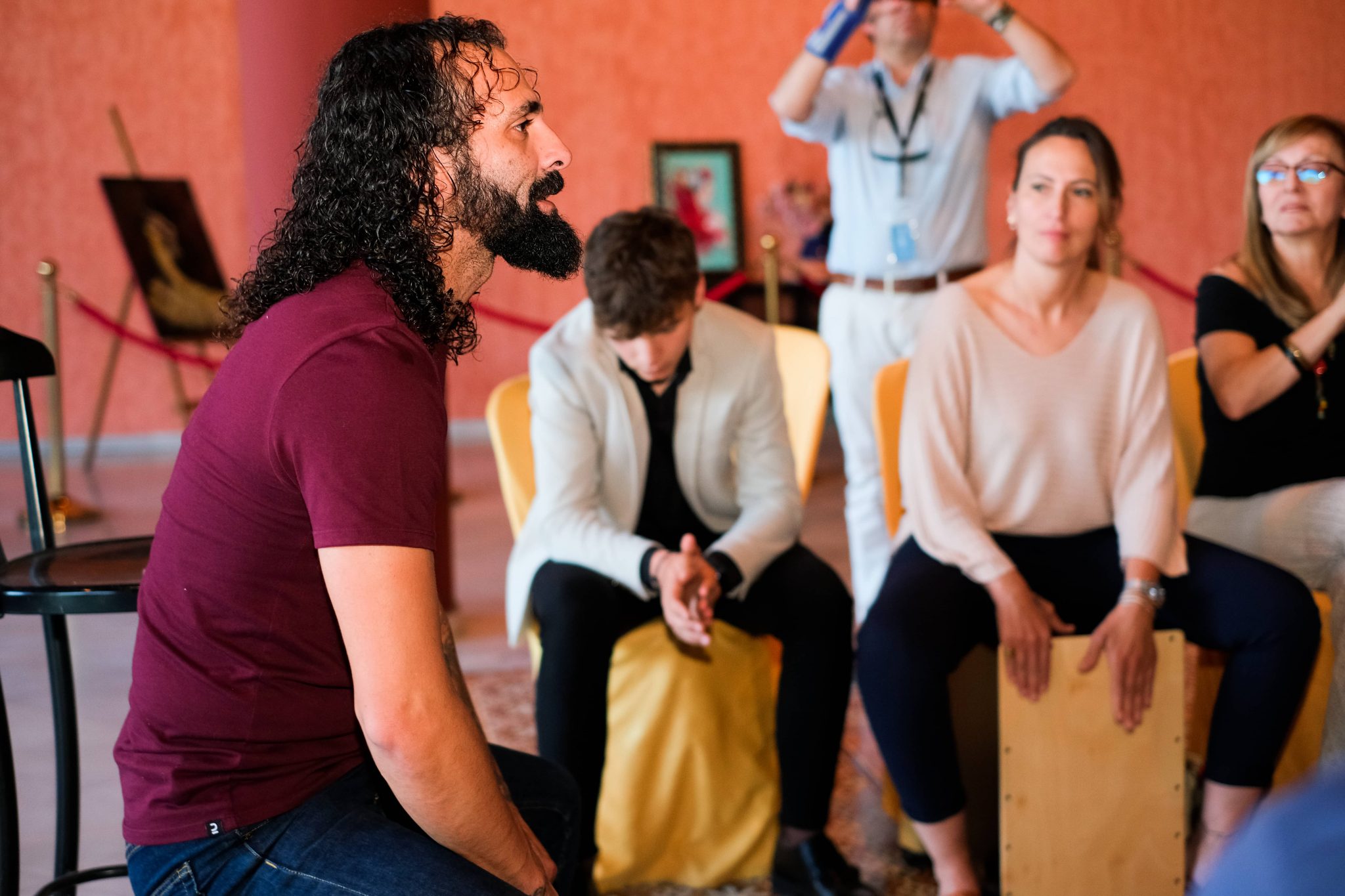 Man with curly hair sitting in front of people playing percussion instruments.