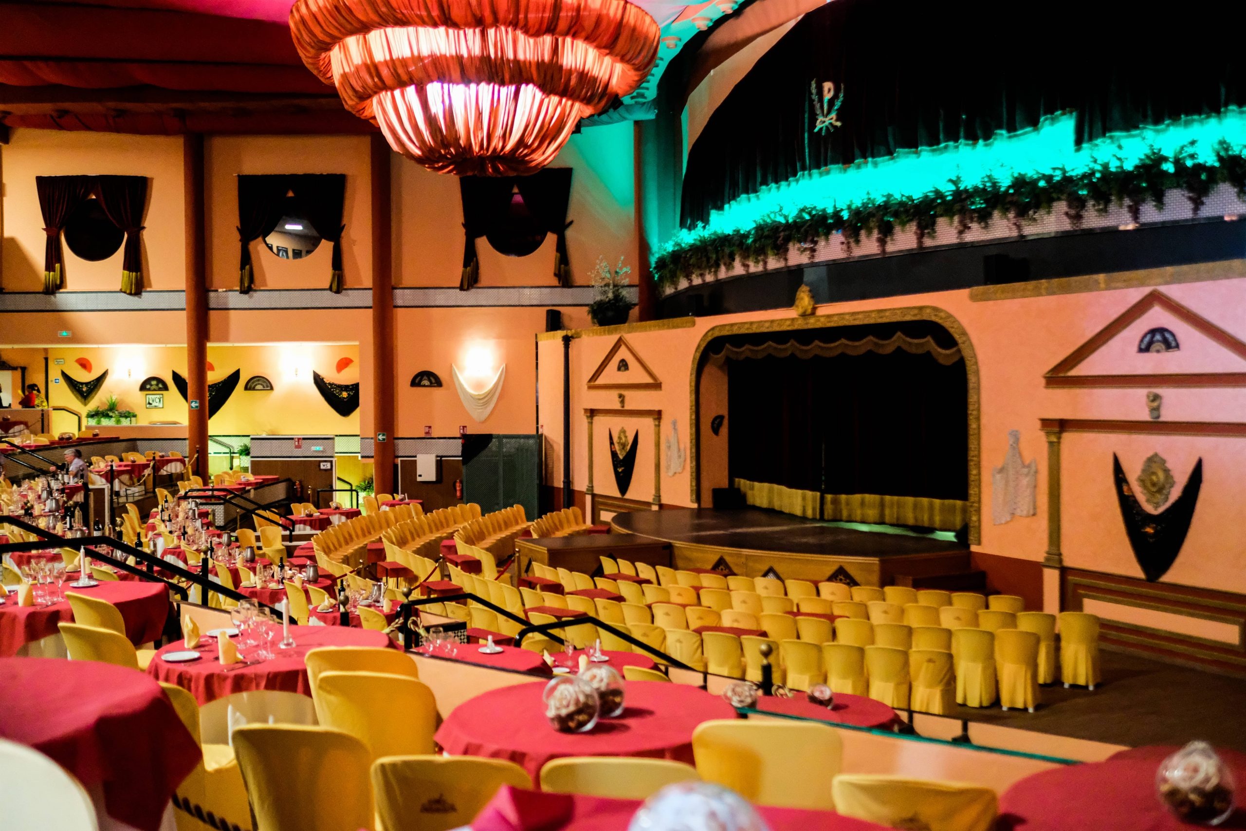 Colorful cabaret venue with tables, chairs, stage, and decorative lighting.