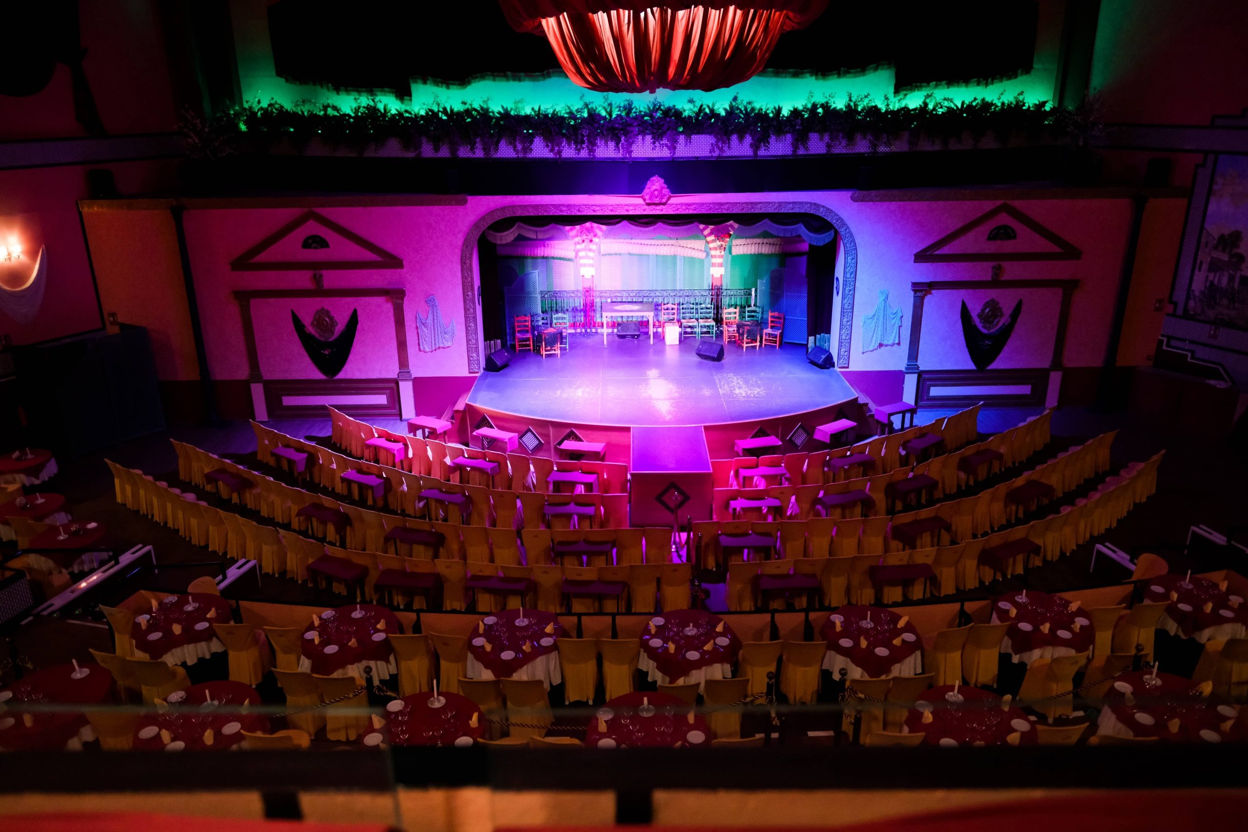 Empty theater with colorful stage lights and arranged dining tables.