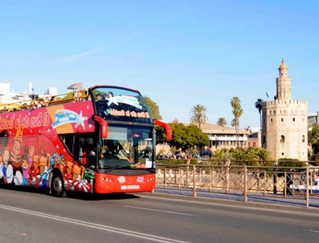 Red double-decker tour bus on a bridge near a historical tower.