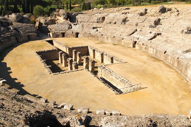 Ancient Roman amphitheater ruins with central stone structures and surrounding seating.