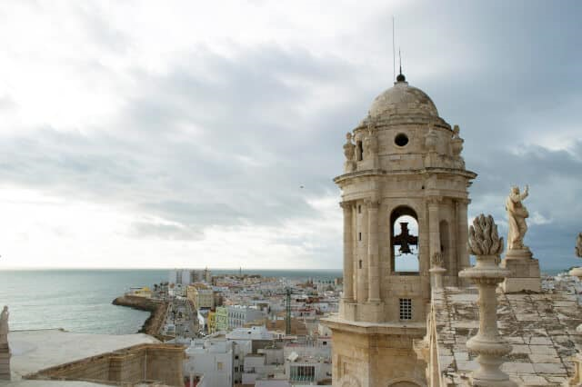 Seaside view with a historic bell tower and statues under a cloudy sky.