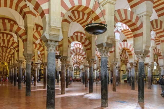 Interior of historic mosque-cathedral with red and white arches, columns, and hanging lights.