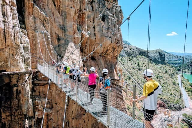 People crossing a suspension bridge on a rocky cliff.