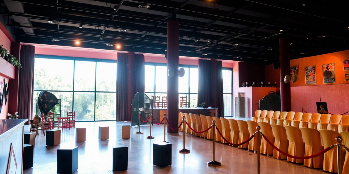 Empty auditorium with red walls, chairs, and large windows.