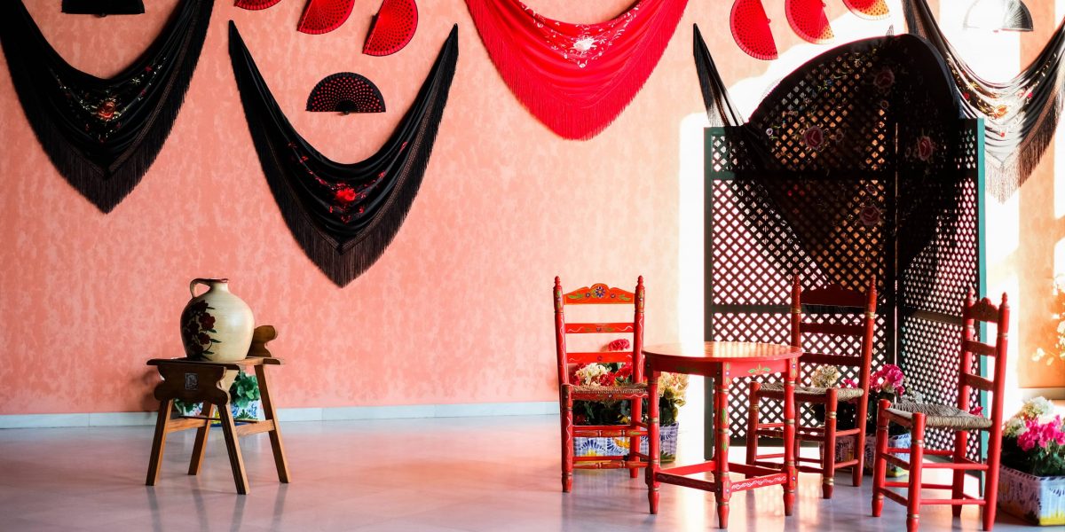 Room with red chairs, a table, and decorative shawls on an orange wall.