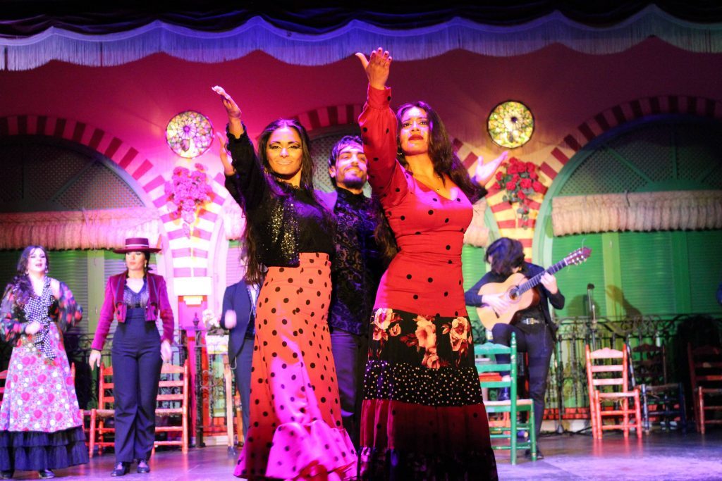 Flamenco dancers in vibrant dresses perform on a colorful stage.