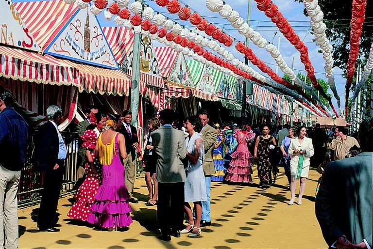 People in colorful costumes at an outdoor festival with decorated tents and hanging lanterns.