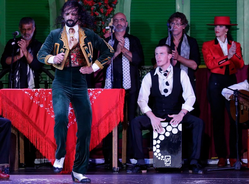 Flamenco dancer performing, surrounded by musicians and a singer on stage.