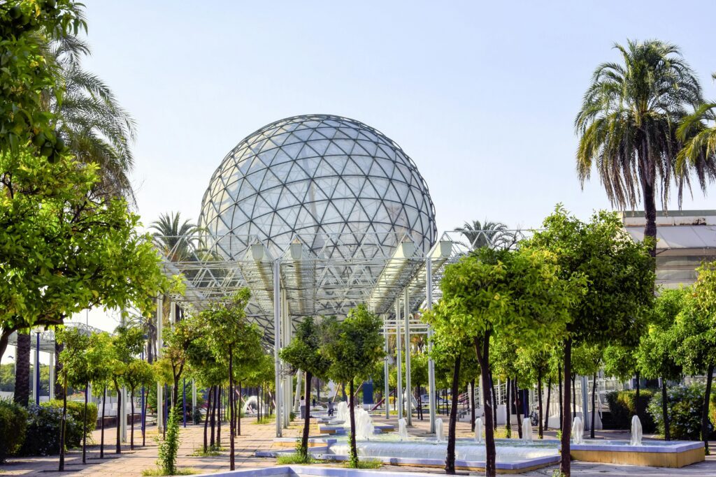 Geodesic dome in garden with palm trees and benches.