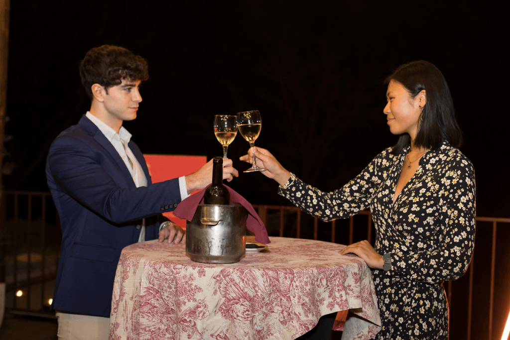Two people toasting with wine over a table with an ice bucket.