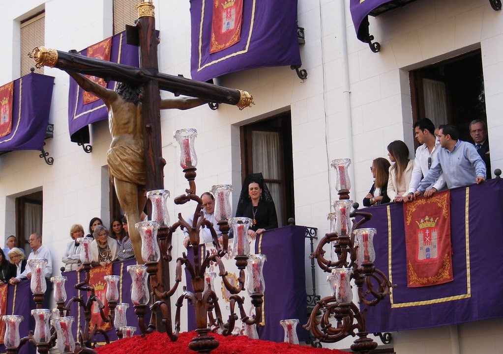 People watch a religious procession from balconies with purple banners.