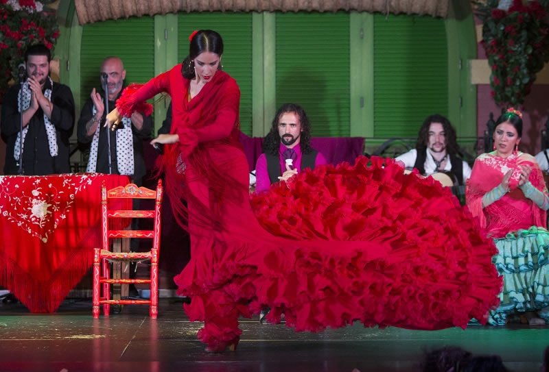 Flamenco dancer in red dress performs with musicians on stage.