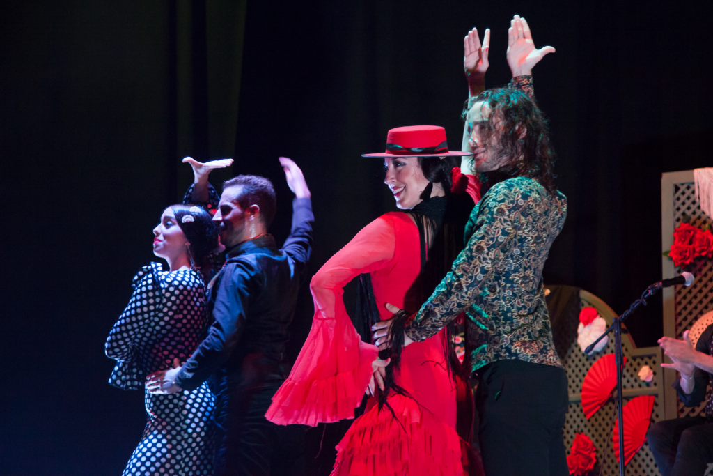 Four dancers in colorful flamenco attire performing on stage.