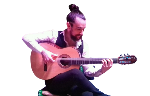 Man with a topknot playing an acoustic guitar while seated.
