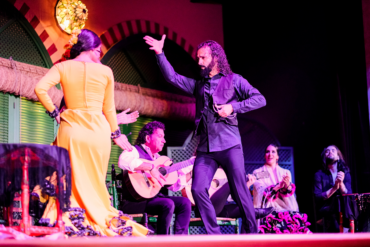 Flamenco dancers perform on stage with musicians playing guitars.