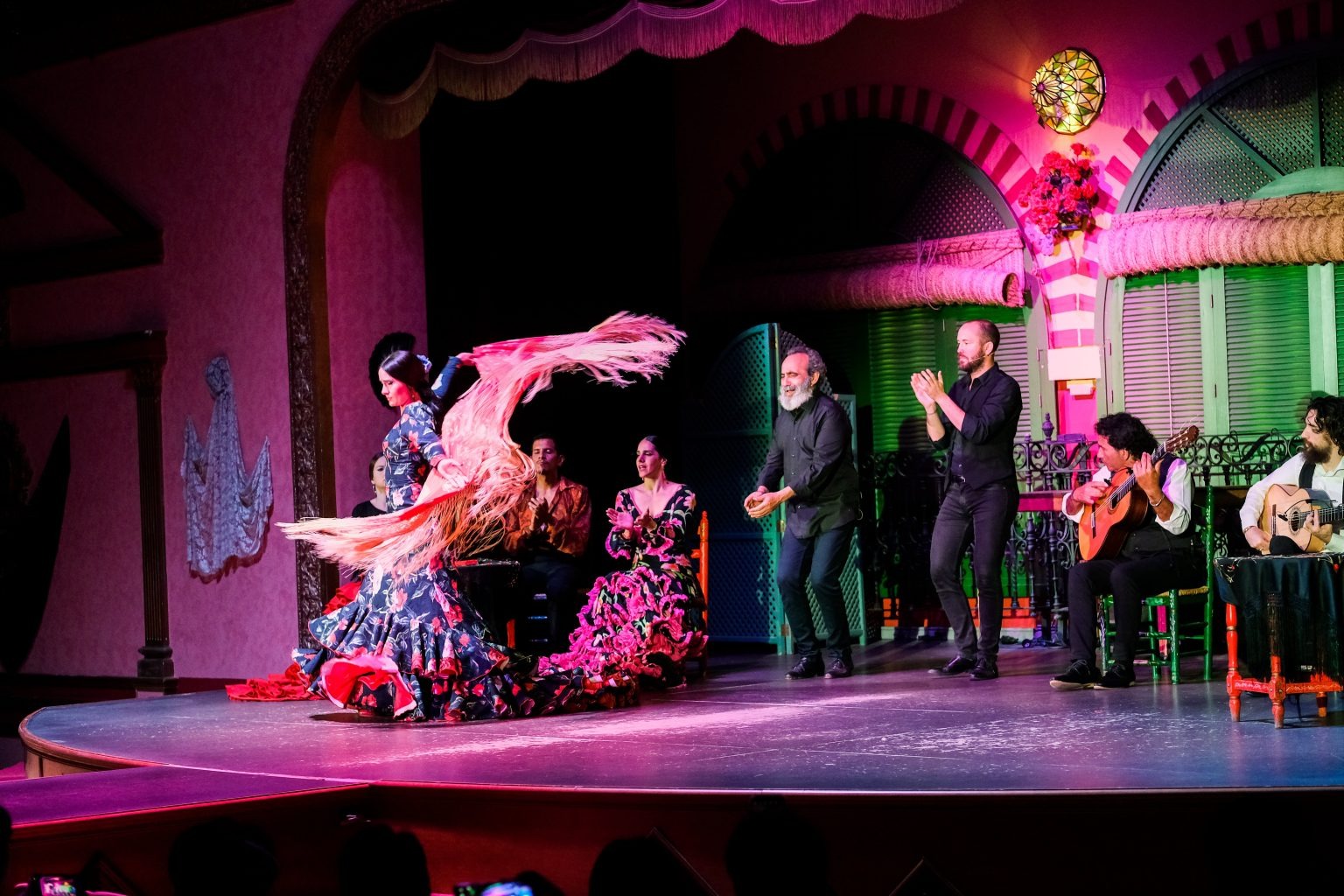 Flamenco dancer twirls on stage with musicians clapping and playing guitar.
