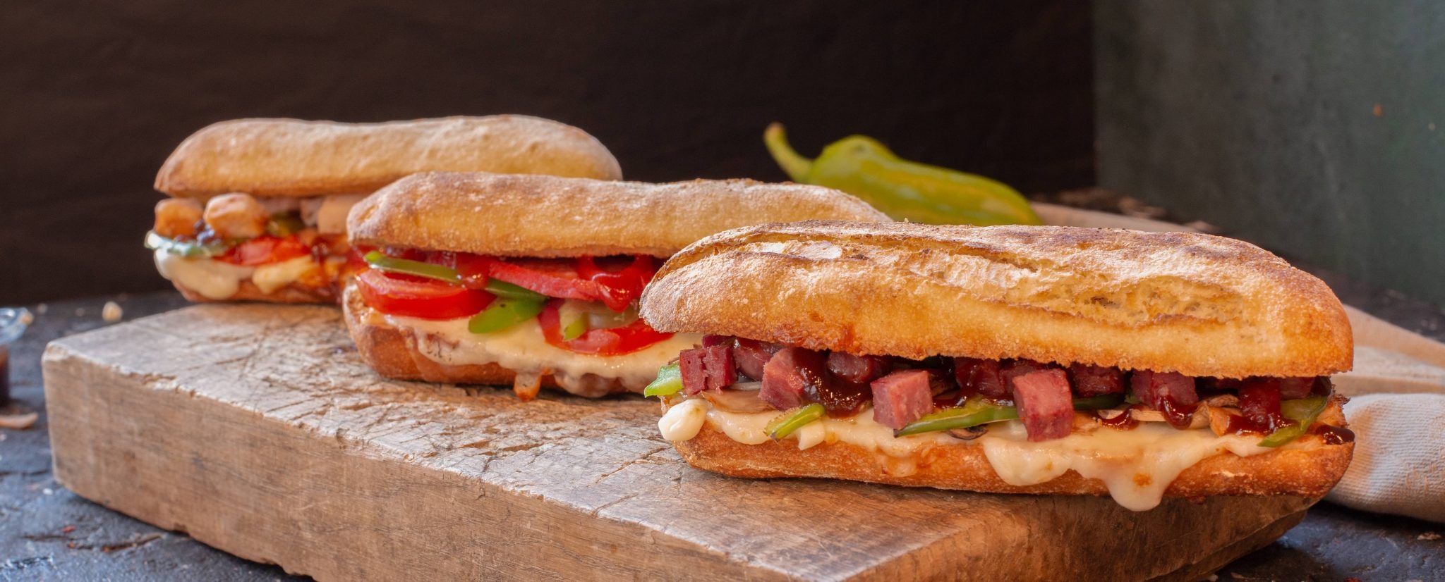 Three panini sandwiches with various fillings on a wooden board.