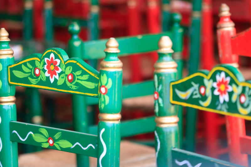 Colorful wooden chairs with floral designs, mostly green with some red, in close focus.