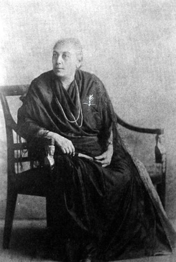 Elderly woman in dark dress seated on chair, holding a fan.