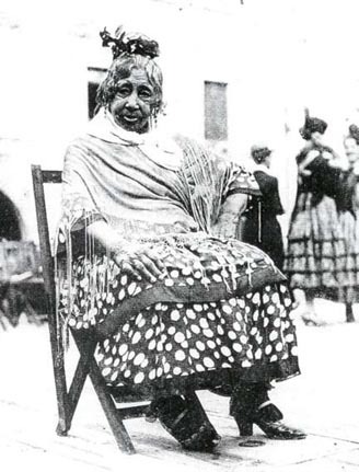 Elderly person in traditional attire sitting on a chair outdoors.